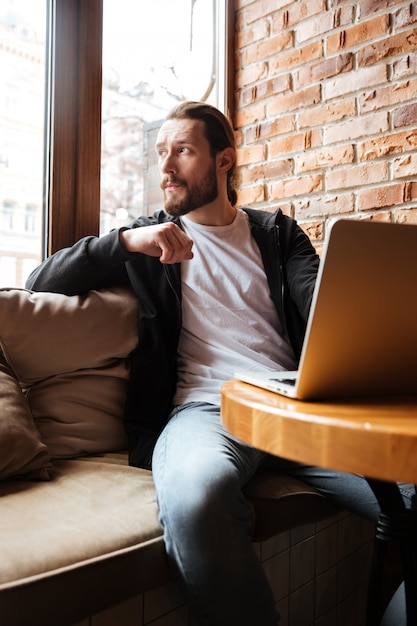 Bearded man using laptop in cafe and looking away