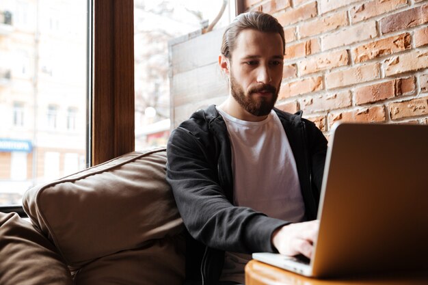 Bearded man using laptop near the window in cafe
