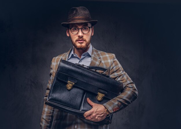 A bearded man wearing casual suit in a hat and glasses holds sui