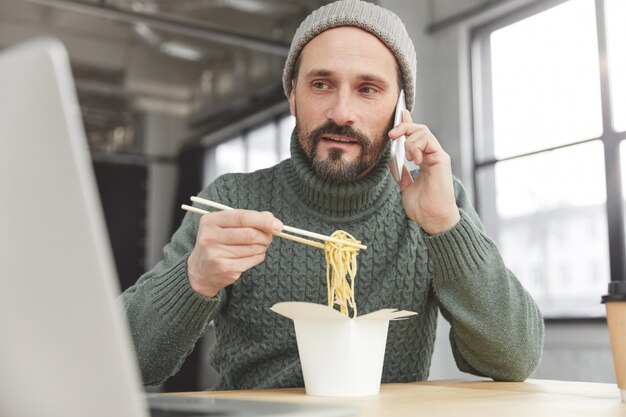 Bearded man wearing knitted warm sweater and hat having lunch