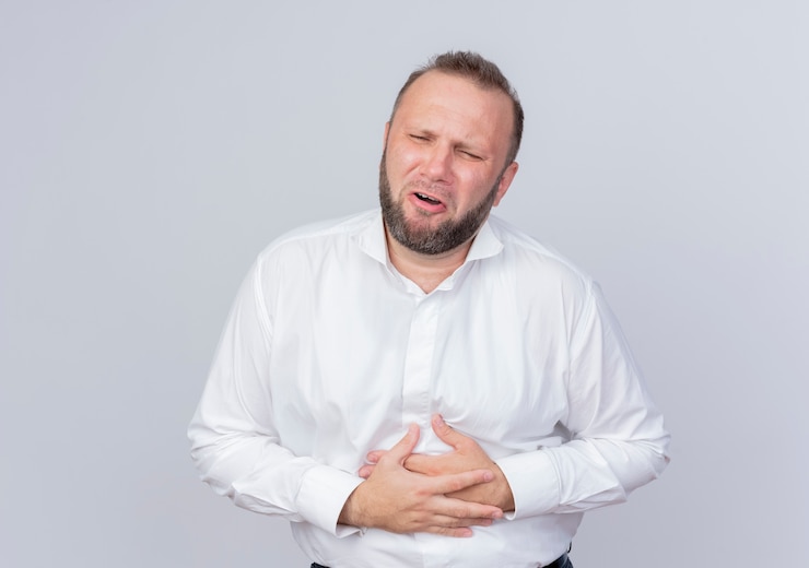 Free Photo bearded man wearing white shirt looking unwell touching his belly having pain standing over white wall