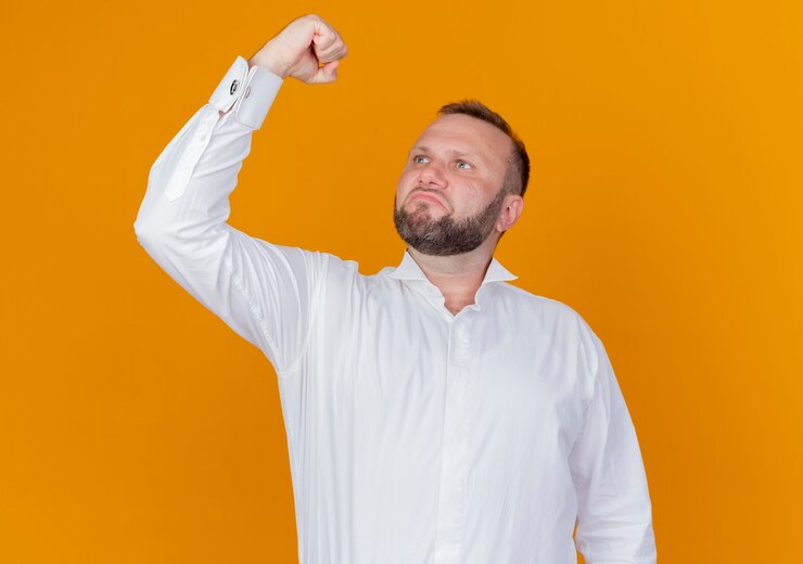 Free Photo bearded man wearing white shirt raising fist looking confident standing over orange wall