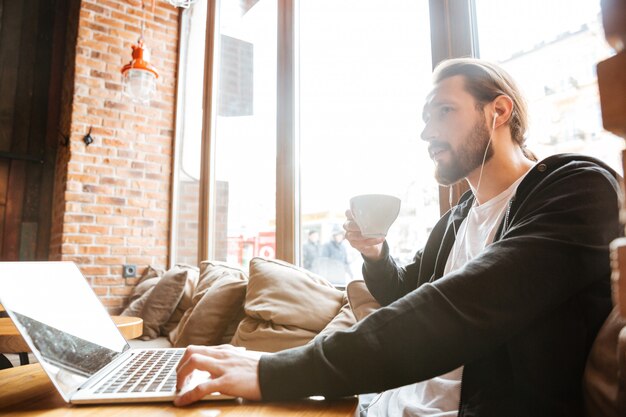 bearded man with laptop drinking coffee in cafe