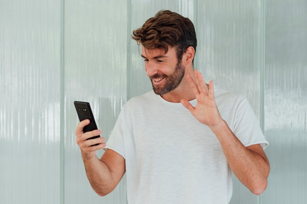 Free photo bearded man with phone waiving at camera