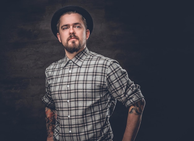 Bearded man with tattooed arms wearing a plaid fleece shirt and a wool vintage hat.