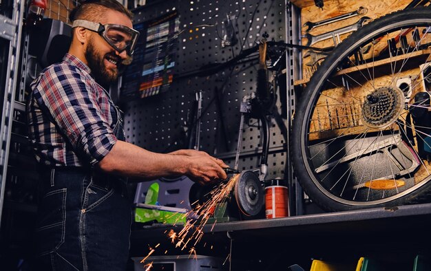 Bearded mechanic cutting and polish bike part in a workshop.