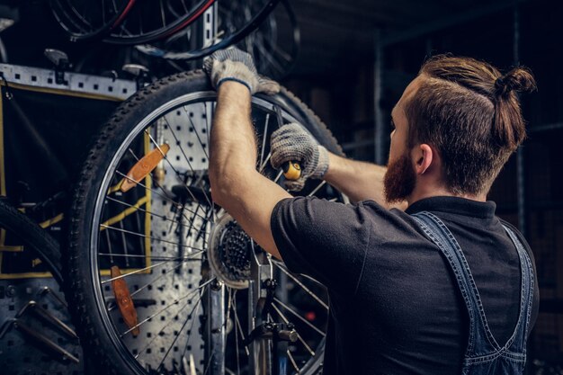 ワークショップで自転車のホイールタイヤを修理するひげを生やした整備士。背面図、サービスマニュアル。