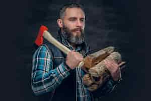 Free photo bearded middle age male holds an axe and firewoods over dark grey background.
