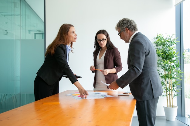 Bearded middle-aged CEO in glasses working with managers and reading report