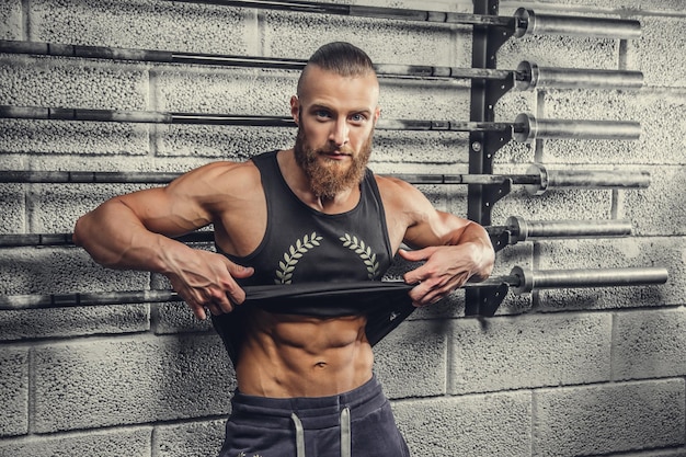 ジムクラブでポーズをとる灰色のTシャツを着たひげを生やした筋肉質の男。