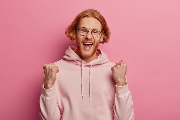 Bearded red haired youngster clenches fists, celebrates success and victory