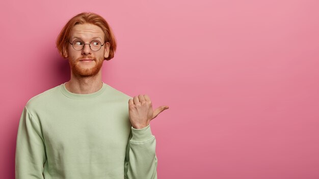 Bearded red head adult man points with thumb to right side