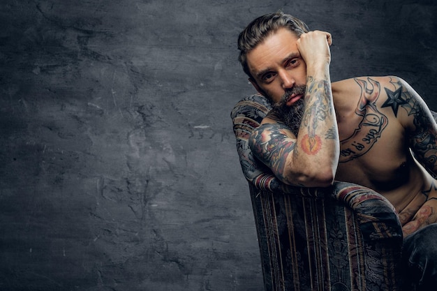 Bearded sad man is sitting in old armchair at abandoned house alone and thinking about his life.