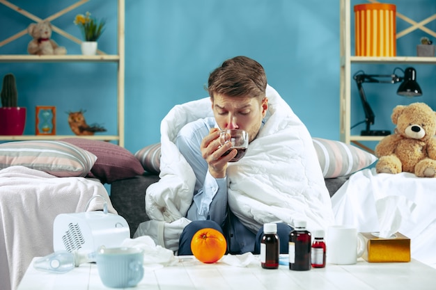 독감이 집에서 소파에 앉아 따뜻한 담요로 덮여 있고 기침에서 시럽을 마시는 수염 난 아픈 남자. 질병, 인플루엔자, 통증 개념. 집에서의 휴식