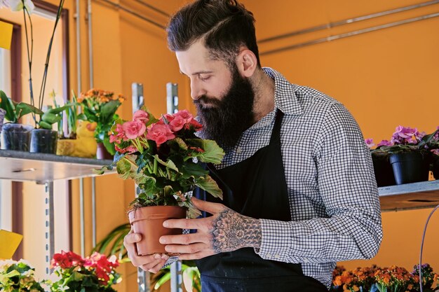 あごひげを生やしたスタイリッシュな花の売り手は、マーケットショップでピンクのバラを持っています。