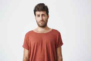 Free photo bearded stylish male having displeased look standing in casual cloth against white wall. young man having some problems looking with unsatisfaction and discontent