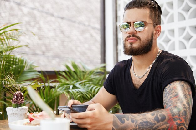 Бородатый стильный мужчина сидит в кафе