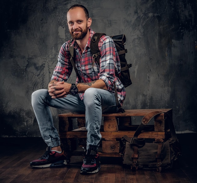 Bearded tattooed backpacker male posing in a studio on grey background.