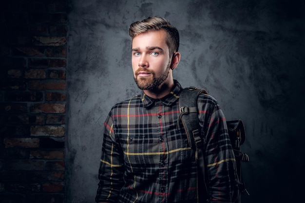 A bearded traveler male dressed in a fleece shirt with backpack posing over grey background.