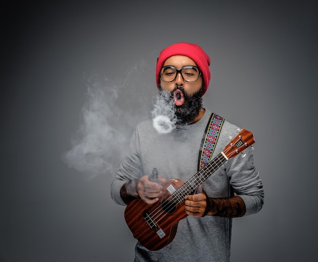 Bearded unformal male holding acoustic small guitar and smoking a cigarette.
