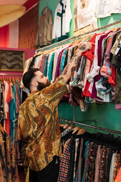 Bearded young man choosing red t-shirt from the rail in the clothing shop