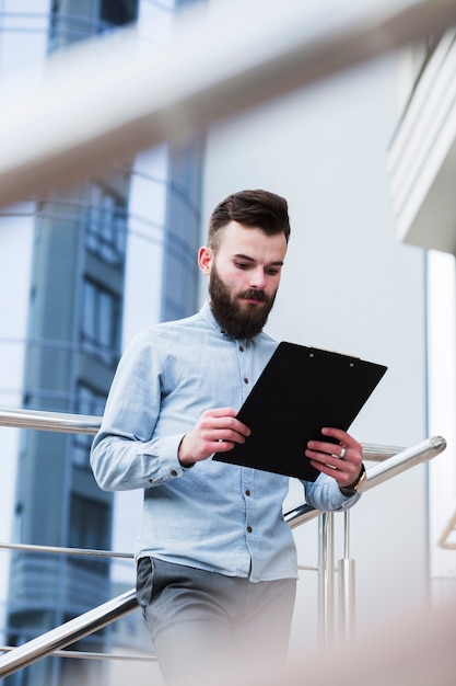 Bearded young man standing in front of railing looking at clipboard