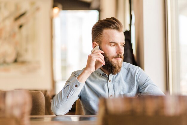 レストランで携帯電話で話すひげのある若い男