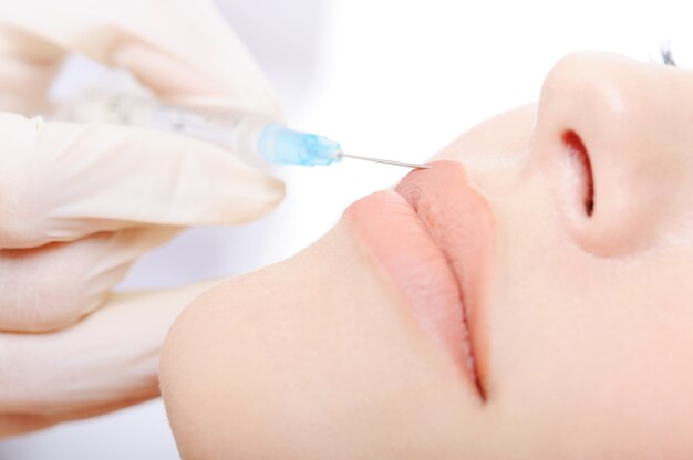 Beautician applying botox shot in the lips of young woman