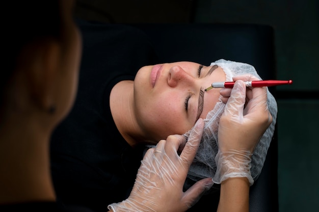 Косметолог делает процедуру микроблейдинга женщине в салоне красоты