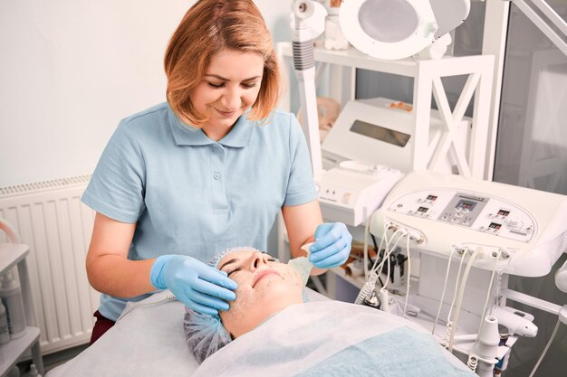 Beautician pulling off cosmetic mask from woman face