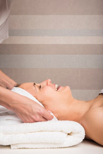 Beautician's hand wrapping towel on smiling young woman's head