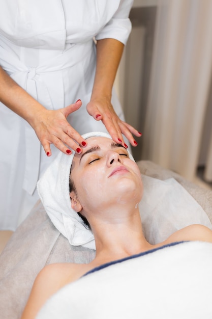 Beautician in a spa beauty salon applies cream to a client's face, a girl lies on a cosmetology table