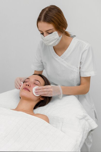 Beautician with female client at salon for face care routine with cleansing disks