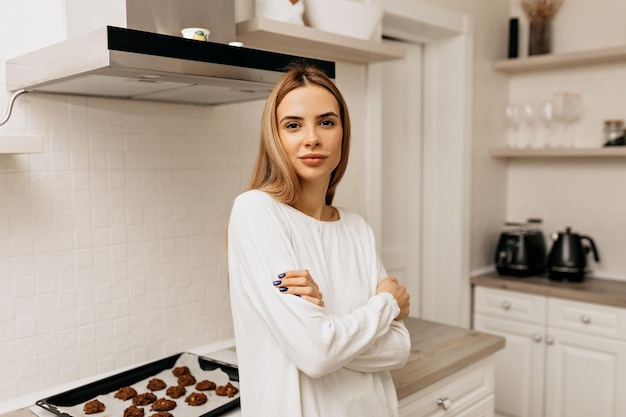 Beautiful adorable lady with light hair and nude make up posing at camera in the kitchen with happy smile woman at home is cooking