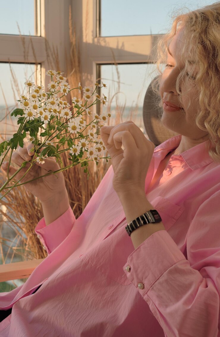 Free Photo beautiful adult blonde woman with a bouquet of daisies sits in a chair twists the petals of a chamomile flower closeup selective soft focus vertical frame