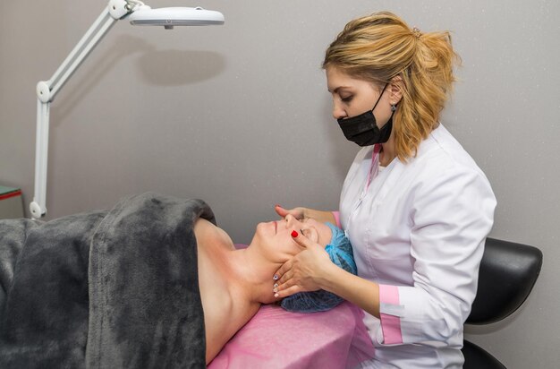 Beautiful adult woman enjoying facial massage at the spa. relaxing medical treatment and beauty concept. beautician in blue gloves makes facial massage to a client