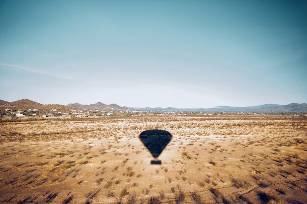 Beautiful aerial shot of a desert field with the shadow of a moving air balloon in the sky