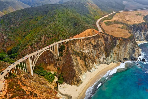 Beautiful aerial shot of green hills and a curvy narrow bridge going along the cliffs