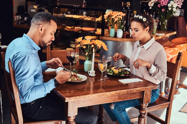 彼らのデートで一緒に素晴らしい時間を過ごしている愛の美しいアフリカ系アメリカ人のカップル、お互いを楽しんでいる魅力的なカップル、レストランで食事をしています。