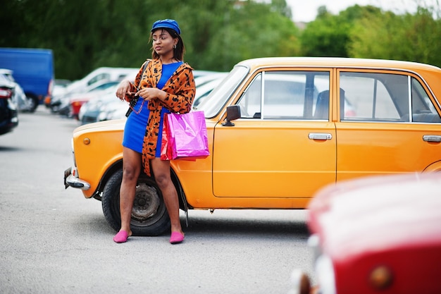 オレンジ色の古典的なレトロな車の近くに立っている買い物袋を持つ美しいアフリカ系アメリカ人の女性