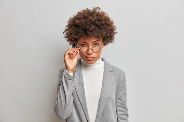 Beautiful African American woman looks attentively through round glasses