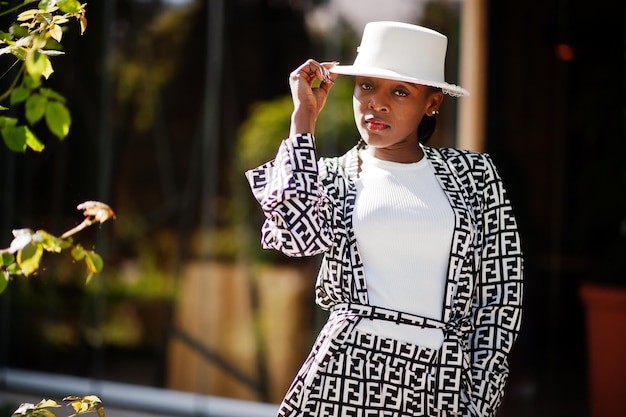 美しいアフリカ系アメリカ人女性のナチュラルメイクはファッション服カジュアルな黒と白のドレスコードオフィススタイルのトータルブラウスとパンツスーツと帽子を着用してください
