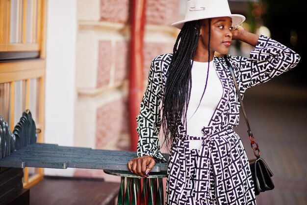 美しいアフリカ系アメリカ人女性のナチュラルメイクはファッション服カジュアルな黒と白のドレスコードオフィススタイルのトータルブラウスとパンツスーツと帽子を着用してください