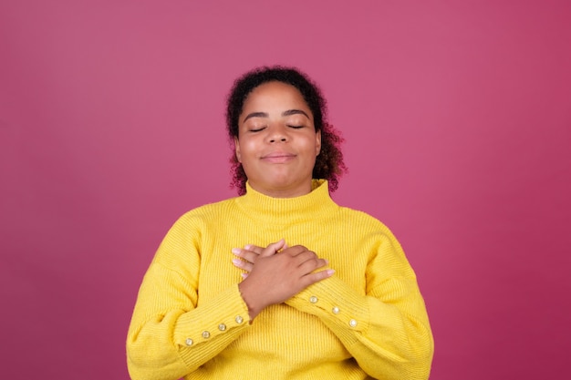 Красивая афро-американская женщина на розовой стене, счастливые улыбающиеся руки на груди, концепция любви, самообслуживания