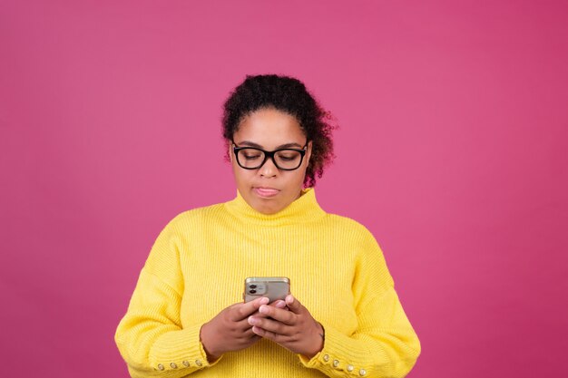 ピンクの壁に美しいアフリカ系アメリカ人の女性が携帯電話でメッセージを入力することに焦点を当てた思慮深い