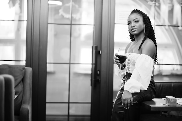 Free photo beautiful african american woman in white blouse and red leather pants pose at restaurant with glass of wine