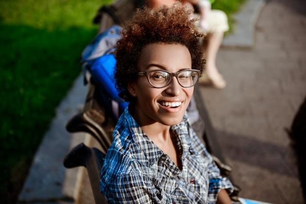 Bella ragazza africana sorridente, ammiccanti, seduto sulla panchina nel parco.