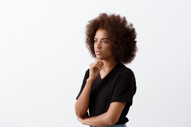 Beautiful african girl thinking over light wall.