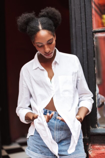 Beautiful african girl with dark curly hair in white shirt and denim shorts thoughtfully closing eyes isolated