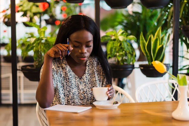 Beautiful african woman is making notes in cafeteria